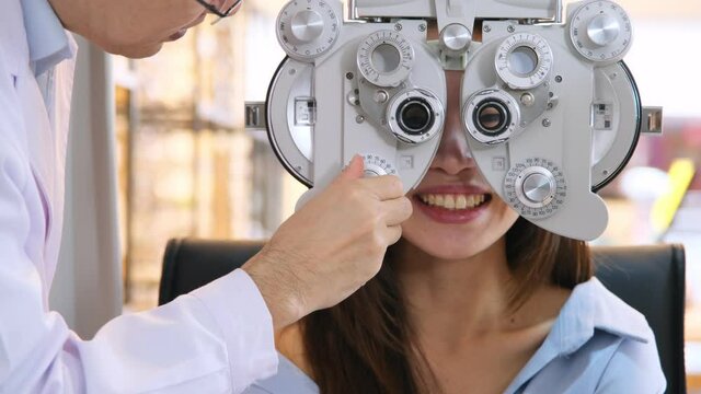 Ophthalmologist examing eyesight measurement to young woman with optical phoropter at eyeglasses shop.