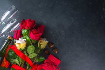 Valentines day greeting card concept with red rose flowers, champagne, chocolates and gift box. Top view flat lay on black concrete background with space for greetings