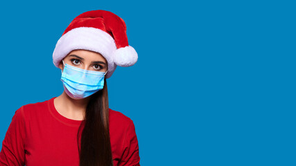 Caucasian woman in protective medical mask and Santa hat on blue isolated background. Christmas on quarantine.