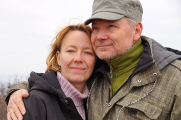 Smiling middle-aged man and woman standing hugging in nature