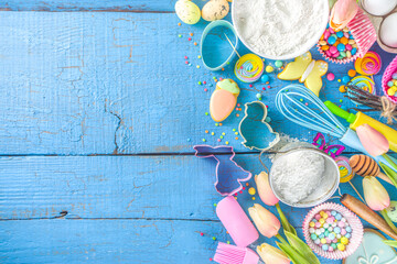Easter baking background with rolling pin, whisk, eggs, flour and colorful sugar confetti on blue wooden table top view. Flat lay with copy space for text