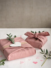 Gift wrapped in pink linen decorated with eucalyptus on a background of paper pink hearts on a white background in the morning light