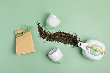 White ceramic tea pot with dry green tea leaves and paper bag on pastel background. Eco friendly...