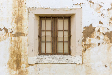 Fototapeta na wymiar an old wooden window with metallic protection bars on a white wall made of clay