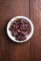 Fresh ripe grape berries in bowl on brown wooden background, top view