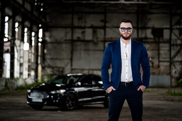 Elegant young handsome man. Fashion portrait of businessman on abandoned warehouse background. Fashion car on the background.