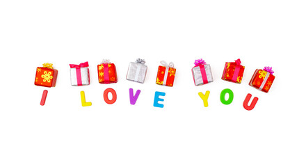 Words I Love You are laid out with colorful letters from the children alphabet puzzle. Above each letter is a gift in form of a festive box tied with red and white ribbon with bows. Flatlay, top view