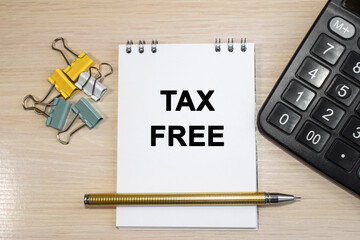 Tax-free written on a notepad that lies on a wooden table near a calculator and stationery clips. Business and financial concept