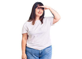 Fototapeta premium Young plus size woman wearing casual clothes very happy and smiling looking far away with hand over head. searching concept.