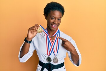 Young african american girl wearing karate kimono and black belt smiling happy pointing with hand and finger © Krakenimages.com