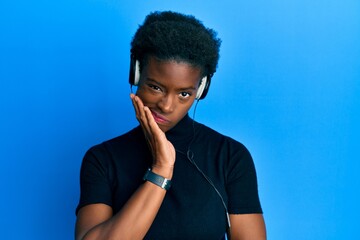 Young african american girl listening to music using headphones thinking looking tired and bored...