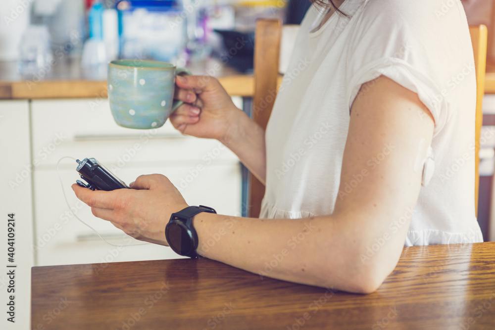 Wall mural Modern diabetes treatment, relaxed woman is operating insulin pump in the kitchen while having a cup of tea