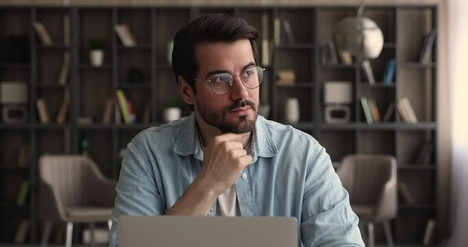 Pensive business man in glasses distracted from laptop work pondering looks in distance. Thoughtful employee search creative ideas, think on challenge seated at desk. Planning, business vision concept
