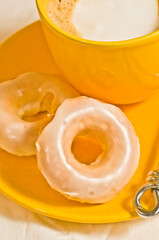top view, close distance of frosted, baked buttermilk donuts and yellow cup of cappuccino, on a yellow plate