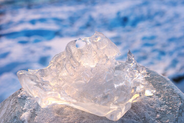 A piece of ice of unusual shape in the sunlight, against the background of a frozen river. Close-up, side view. Space for text