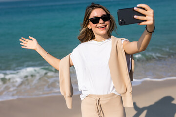 Young woman in summer casual clothes taking a selfie on the phone at the beach