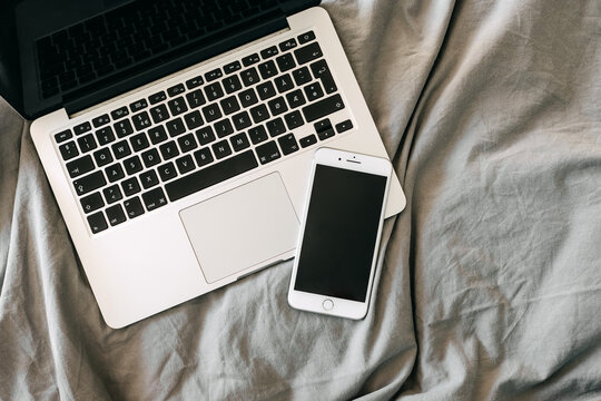 Apple Laptop And IPhone On Gray Bed Sheet Background.