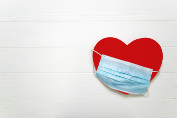 Red heart with blue disposable protective mask on white textured wooden background with copy space. Valentines Day in new normal pandemic time. Health and heart care, medicine, covid 19, coronovirus.