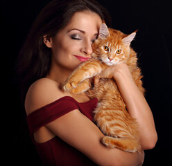 Happy young woman holding and hugging with love her red maine coon kitten with closed enjoying eyes. Closeup portrait