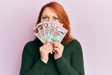 Beautiful redhead woman holding 100 new zealand dollars banknote skeptic and nervous, frowning upset because of problem. negative person.