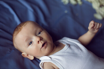 baby boy blonde in white bodysuit lying on the bed