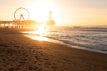 Silhouettes of walking People  at the Beach, with a beautiful Sunset behind a ferris wheel and the...