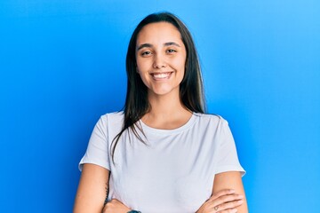 Young hispanic woman wearing casual white t shirt happy face smiling with crossed arms looking at the camera. positive person.