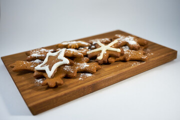 Ginger biscuits with sugar powder on a wooden board on a white background.