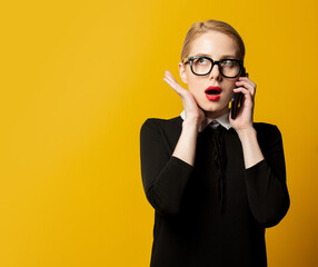 Surprised woman in black formal clothes with mobile phone on yellow background