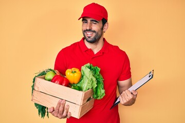 Handsome hispanic man with beard wearing uniform holding delivery food winking looking at the...