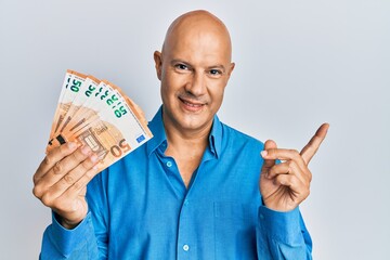 Middle age bald man holding 50 euro banknotes smiling happy pointing with hand and finger to the side