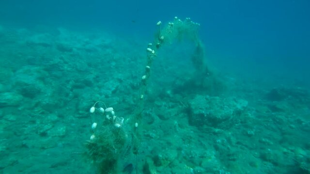 Lost fishing net with buoys lies underwater on the seabed. Problem of ghost gear - any fishing gear that has been abandoned, lost or otherwise discarded. It is the most harmful form of marine debris