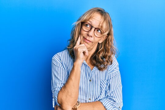 Middle age blonde woman wearing casual clothes and glasses with hand on chin thinking about question, pensive expression. smiling and thoughtful face. doubt concept.