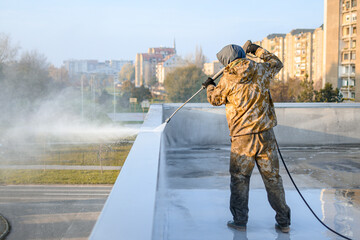 Photography of roof cleaner in yellow uniform. He is washing top of building from dirt. Cityscape is visible in the background. © Branimir