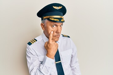 Handsome middle age mature man wearing airplane pilot uniform pointing to the eye watching you...