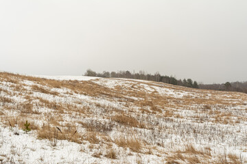 Hills with dry grass are covered with snow. Gloomy winter day. Nature background