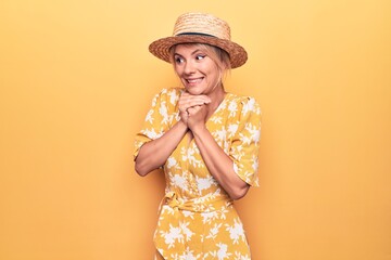 Beautiful blonde woman on vacation wearing summer hat and dress over yellow background laughing...