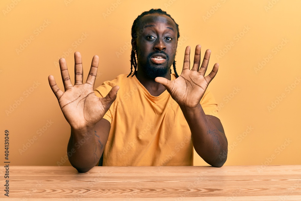 Sticker handsome young black man wearing casual clothes sitting on the table afraid and terrified with fear 