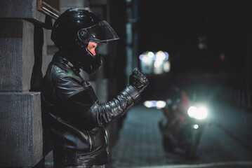 Motor biker in the black leather jacket on the city street at night.