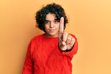 Young hispanic woman with curly hair wearing casual winter sweater pointing with finger up and angry expression, showing no gesture