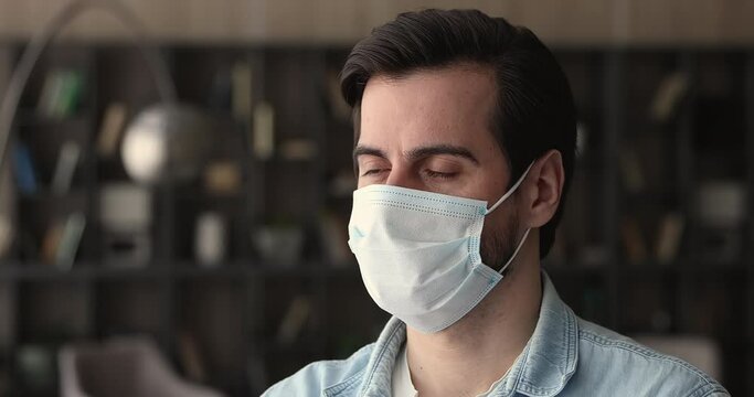 Serious concerned young man standing indoor wear protective surgical face mask look into distance thinking about new reality future. Personal self protection due corona virus pandemic outbreak concept