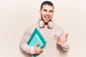 Young handsome man holding book using headphones smiling happy pointing with hand and finger