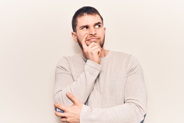 Young handsome man wearing casual sweater serious face thinking about question with hand on chin, thoughtful about confusing idea