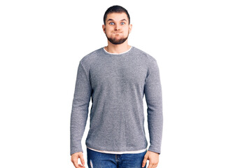 Young handsome man wearing casual sweater puffing cheeks with funny face. mouth inflated with air, crazy expression.