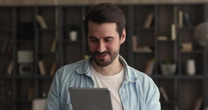 Businessman hold digital tablet in hands using business app, texting e-mail standing in modern office room. Modern wireless tech for personal or professional usage, communication, telecommute concept
