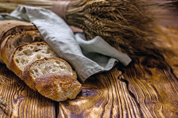 Sliced sourdough bread. A chopped loaf of homemade bread without yeast surrounded by ears of wheat on a dark wooden table. Copy space, vintage style