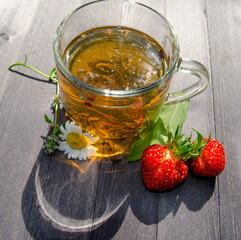 Glass mug of tea with chamomile and strawberries on wooden table
