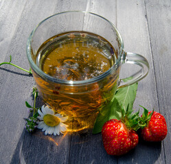 Glass mug of tea with chamomile and strawberries on wooden table
