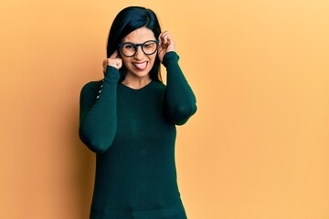 Young caucasian woman wearing casual clothes and glasses covering ears with fingers with annoyed expression for the noise of loud music. deaf concept.