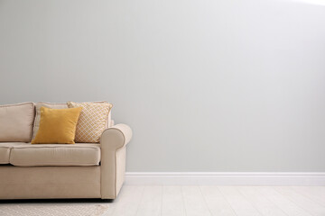 Comfortable beige sofa near light wall indoors, space for text. Simple interior